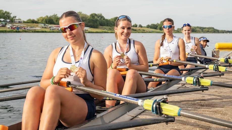 Four girls sit in a boat that has come into dock, showing off their gold medals.