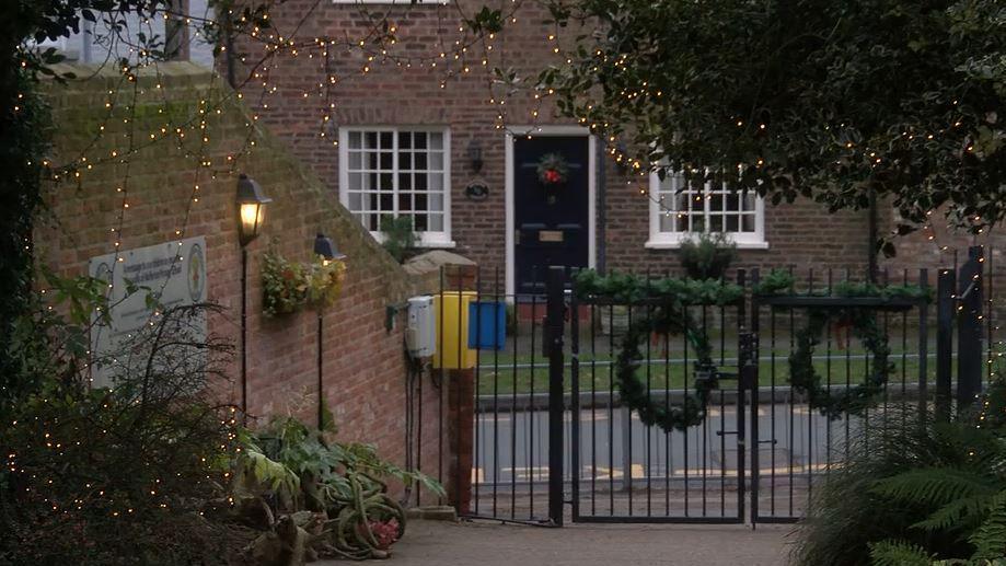 Gates with Christmas wreaths and foliage on. Christmas lights are dangling from the trees.