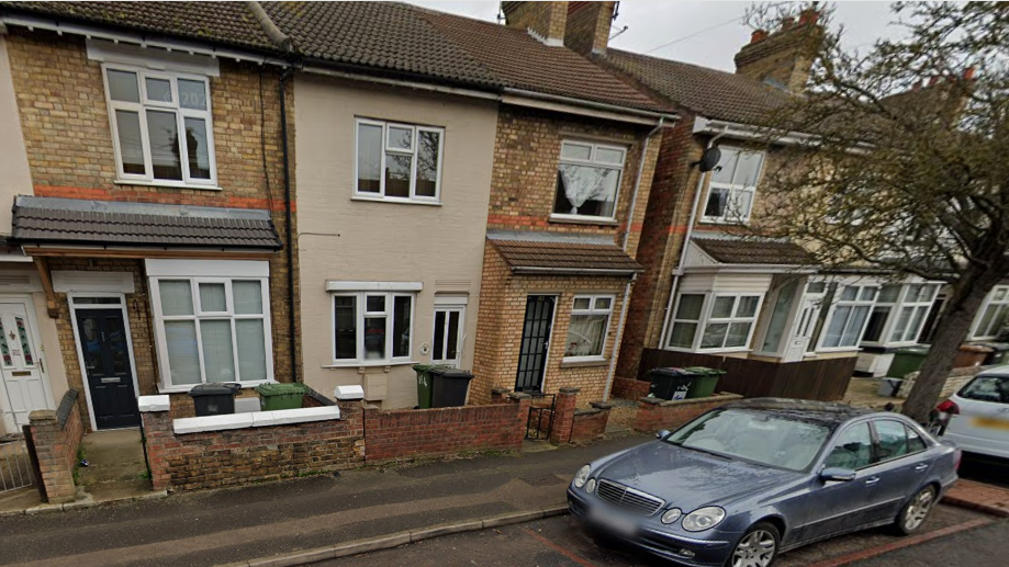 A row of narrow brick-built terraced houses with cars parked in front.