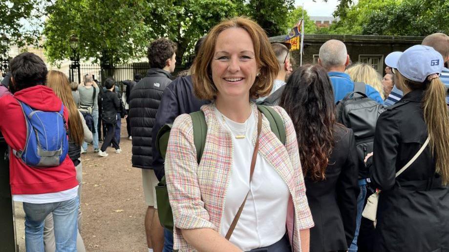 Ms McEvoy, who has a bobbed hair cut, stands as part of a crowd of people looking at buildings in London 