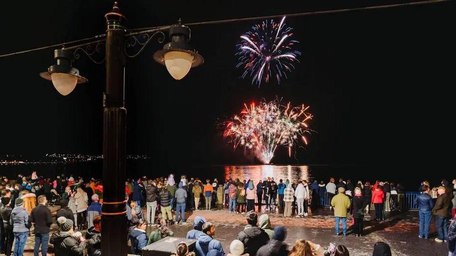 A crowd gathered on a Douglas Promenade at night to watch fireworks being launched from a barge out in the bay. 