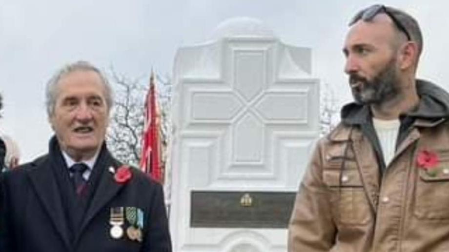Terrance Pringle stands next to Steven Pringle at a Remembrance Day event. His grandad is wearing a dark coloured coat with a poppy and three medals.