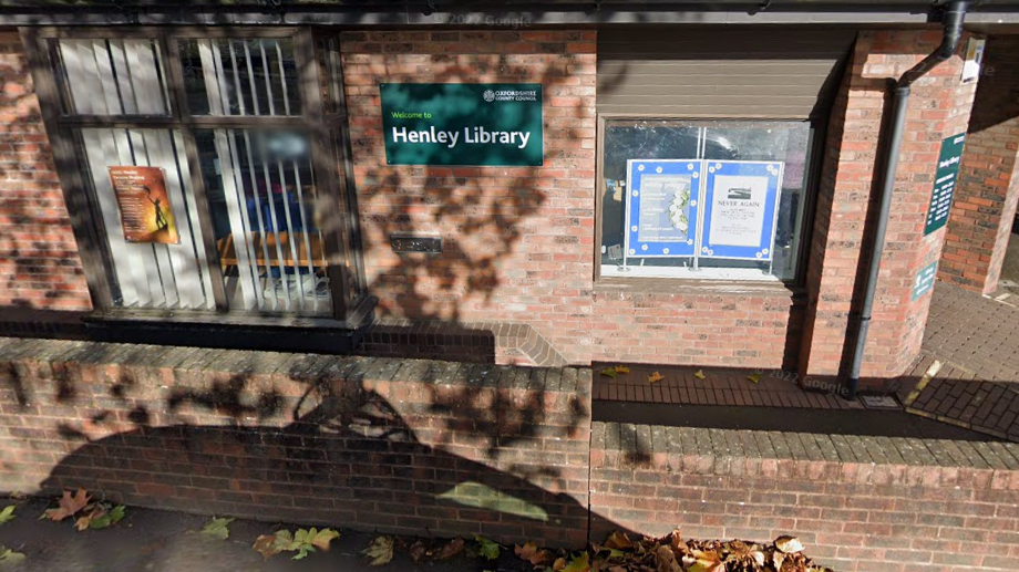 Red brick building with green framed glass doors and a green sign which reads 'Henley Library' in white writing.