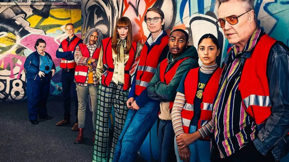 The cast of The Outlaws lined up against a graffitied wall, wearing red hi-vis vests