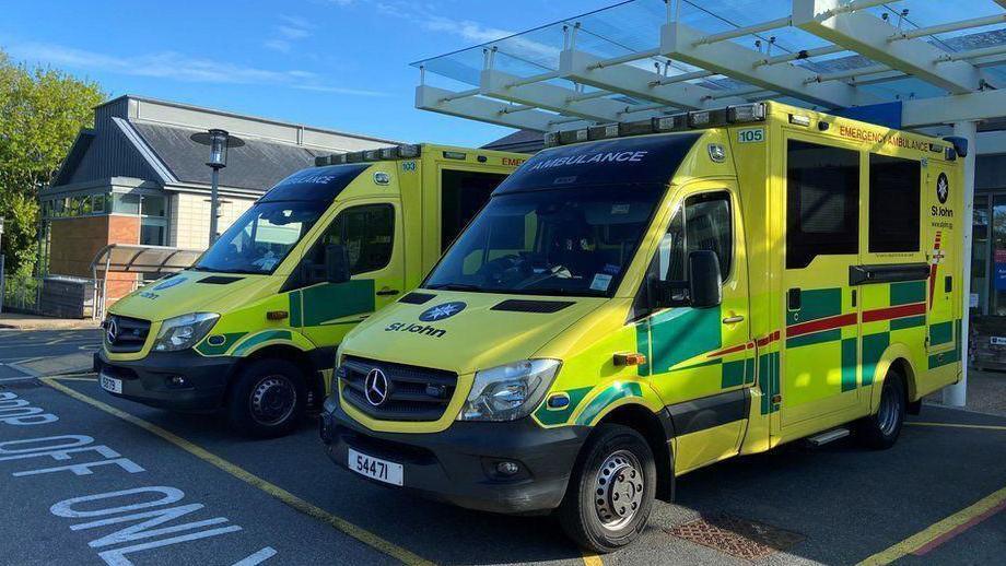 Two ambulances are parked at the hospital in Guernsey. The two vehicles are painted in bright yellow and green colours.