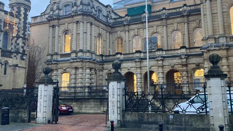 Reading Crown Court: a brown stone building with lighted windows behind a black metal fence.