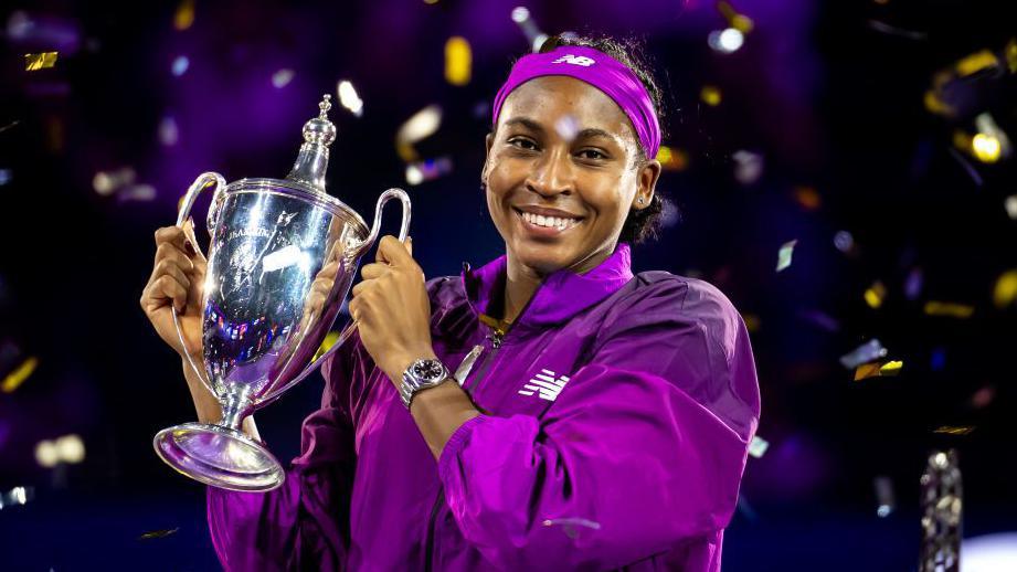 Coco Gauff smiles and holds up the Billie Jean King Trophy