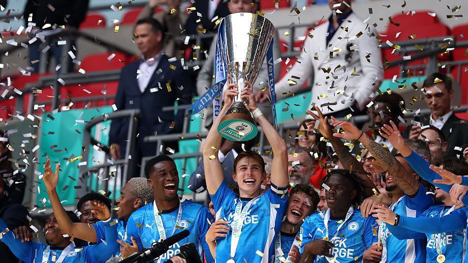 Peterborough United players celebrating winning the EFL Trophy as confetti rains down from above