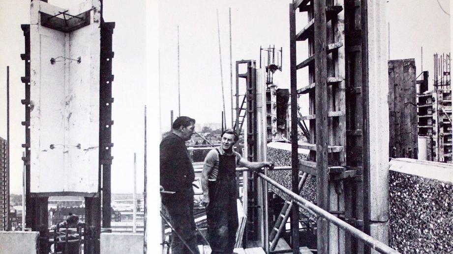Black and white photo showing one of the walls of the tower with two men by the side of the scaffolding talking to each other.