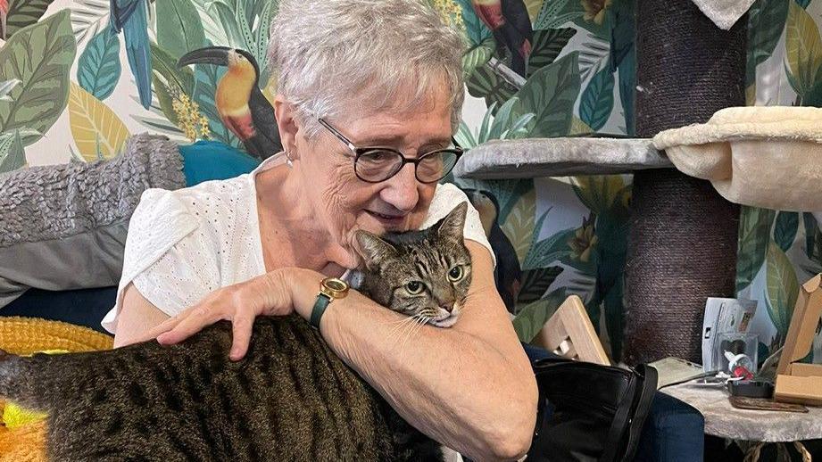 Susan holding her tabby cat on her lap as she sits on a sofa