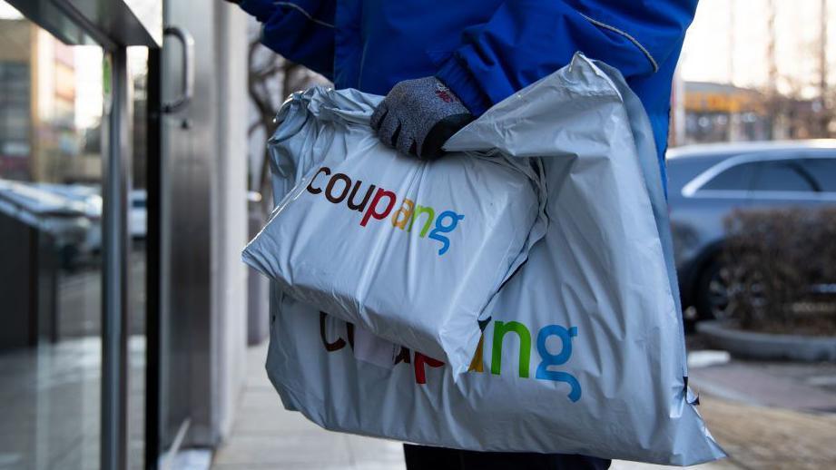 A Coupang employee holds packages in front of an apartment building in Bucheon, South Korea