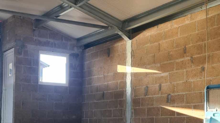 The inside of a new building, show brickwork, a window, a metal steel frame, a roof and a white door to the left. 