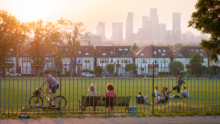 People sitting on a bench and cycling in a park outside of London on a sunny day