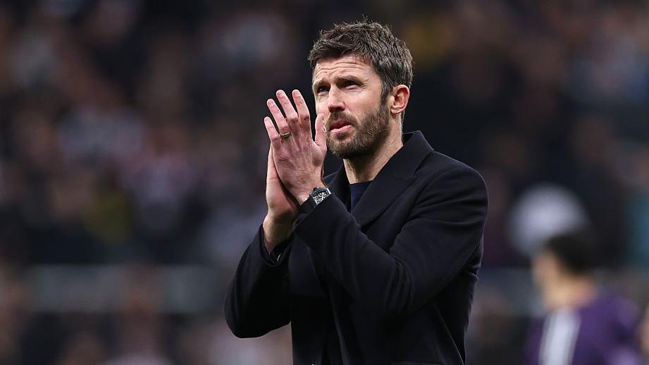 Michael Carrick, in a dark coat, applauds Manchester United fans