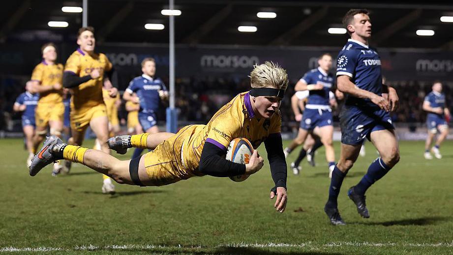 Henry Pollock flying in a dive over the tryline while holding the ball under one arm close to his chest about to score a try