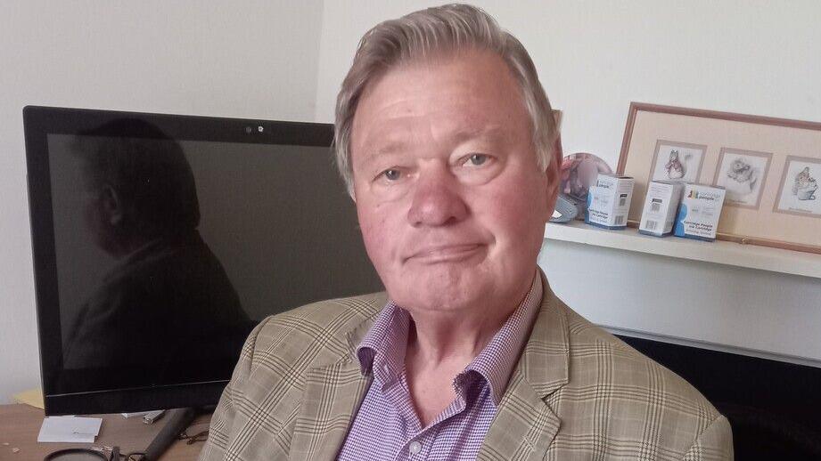A photo of Hamish Brown. He is wearing a blazer over a shirt. He is sitting in front of a computer screen but is looking directly into the camera.