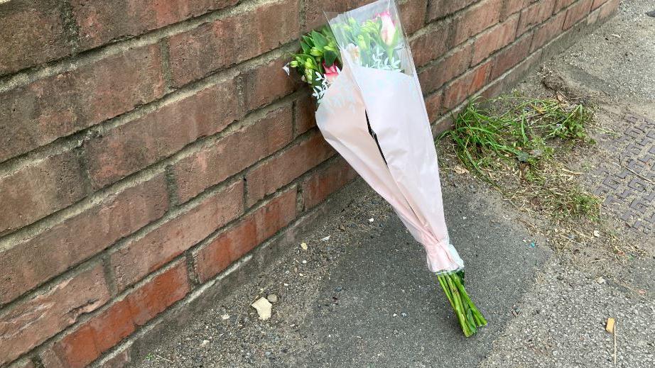 Single bunch of flowers rests against a brick wall near to the police cordon