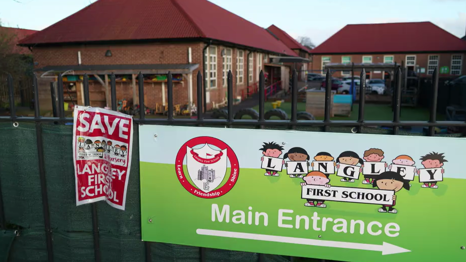 A general view of the entrance to Langley First School. On the railings outside there is a large banner pointing to the school's entrance and a poster saying Save Langley First School.