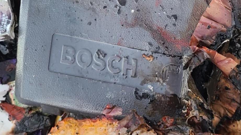 A grey, rectangular object is stamped with the brand name Bosch. It is in a pile of charred cardboard and other waste.