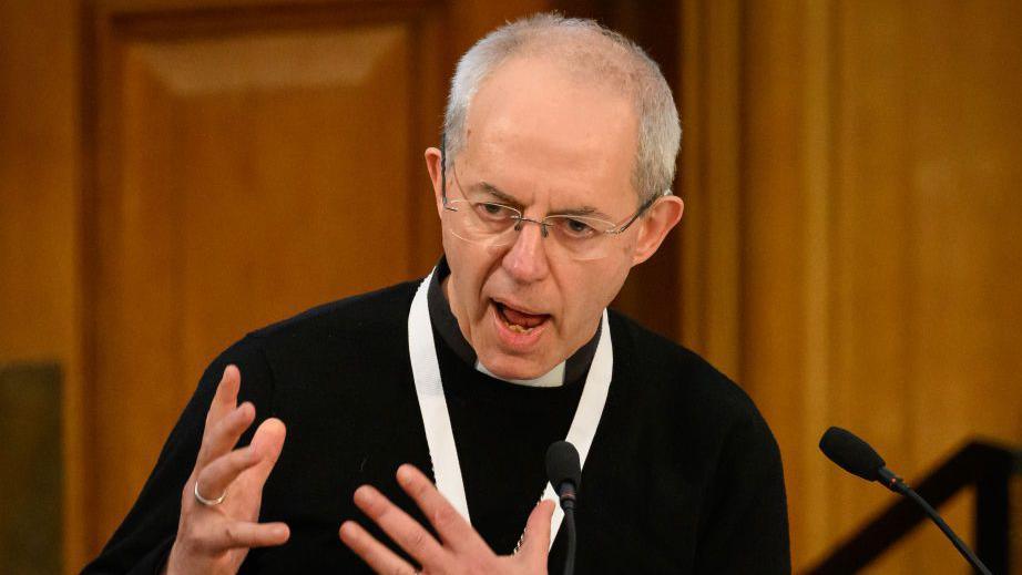 Justin Welby is pictured wearing a black shirt and white dog collar. He is wearing glasses and has short, white hair.