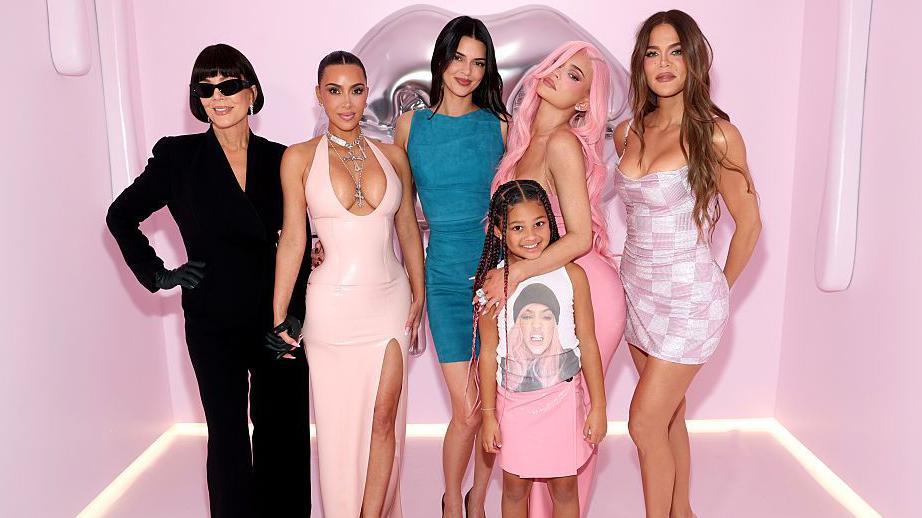 The Kardashian family is pictured posing in front of a pink background