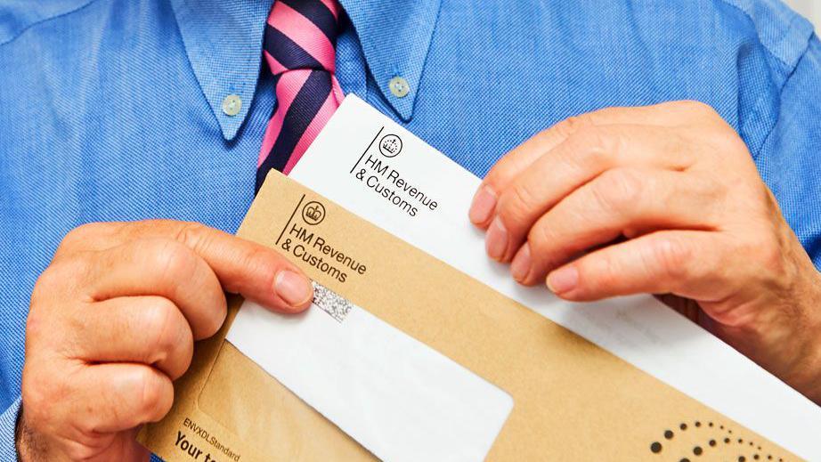 A man's hands hold an HMRC tax envelope