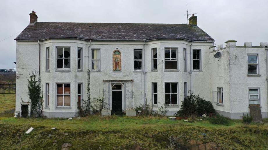 Marianvale mother and baby home from the outside. It is white with some windows broken. There is a stained glass window on the front.