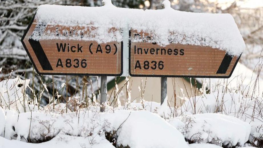 Snow sits on two road signs showing the way to Wick via the A9 on the left and Inverness on the right