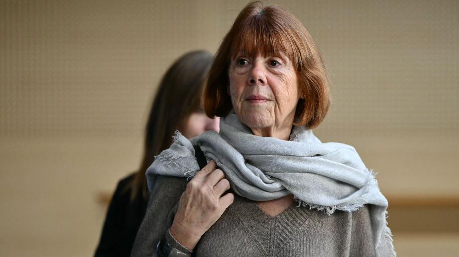 Headshot of a woman with a short brown bob, wearing a grey scarf and a grey V-neck jumper