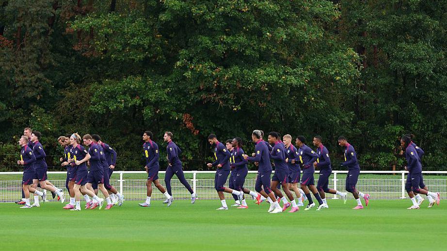 A group of players running across a football pitch during training