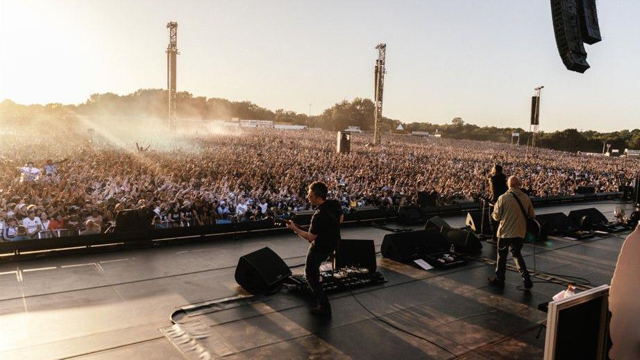 The sun is setting as Noel and Liam Gallagher and Bonehead are seen from behind as they perform in front of a huge crowd at Heaton Park.