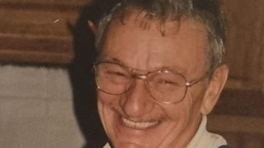 a man with grey hair smiles at the camera and is wearing glasses