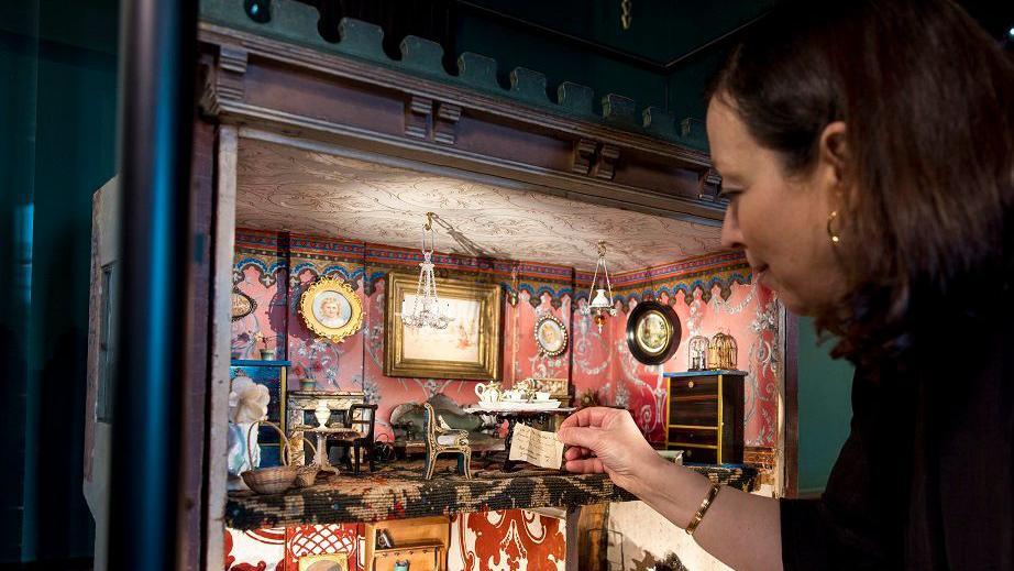 A woman interacting with Beatrix Potter's dolls house. 