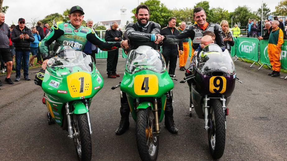 Winner Shaun Anderson on his green racing bike, flanked by John McGuinness and Adam McLean on green and black bikes respectively. People are gathered behind the line up.