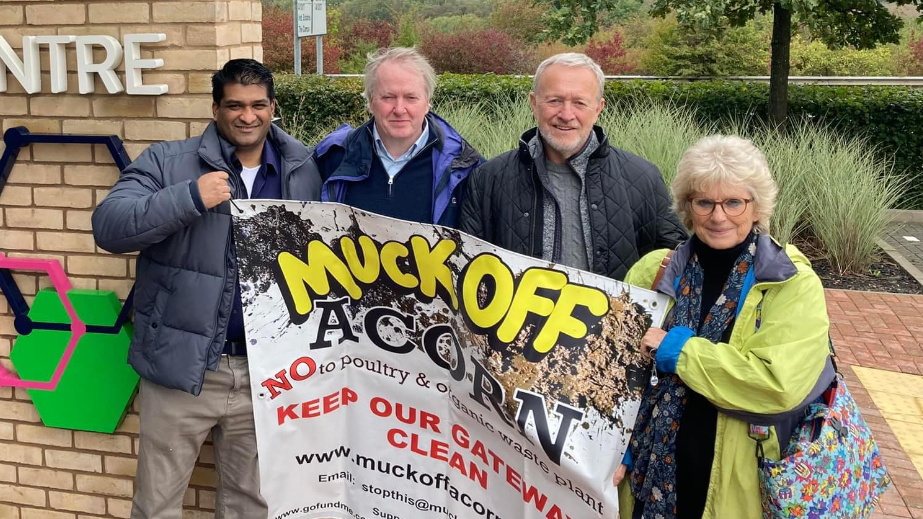 Three men and a woman holding a banner which reads "Muck Off Acorn"