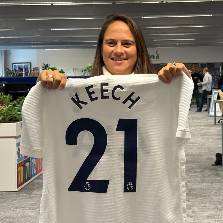 Tina Keech smiles as she holds up a football shirt with her name on the back, and the number 21.