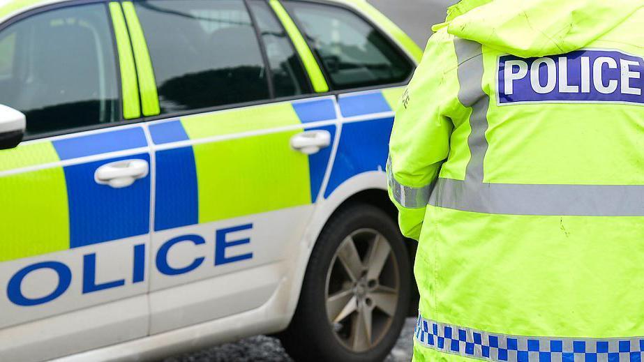 Police officer in high-vis jacket standing in front of police car