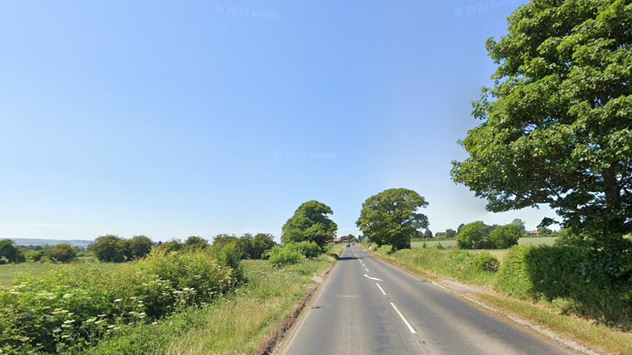 A single carriageway road on a summer's day with green verges and blue sky