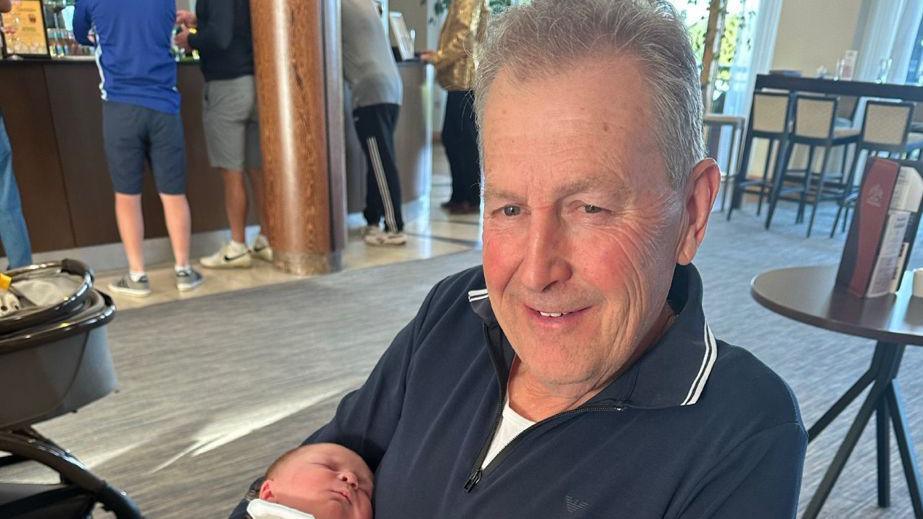 James Messhamsat in a chair in a restaurant holding a baby