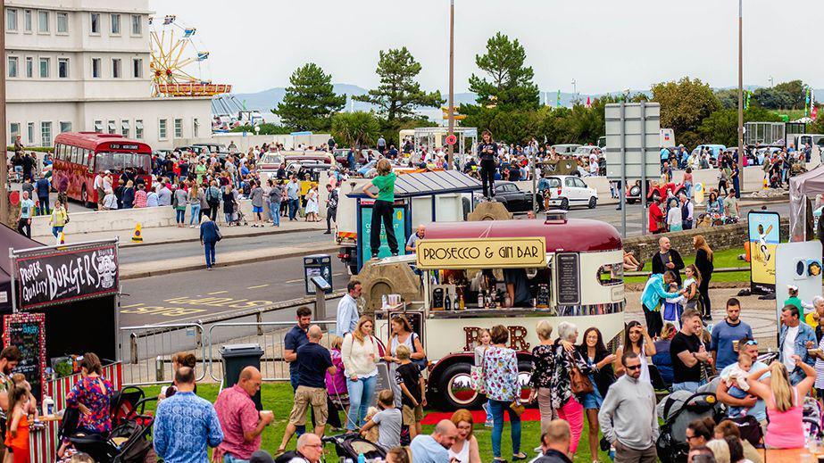 Crowds milling round stalls in Morecambe with Morecambe Bay in the distance