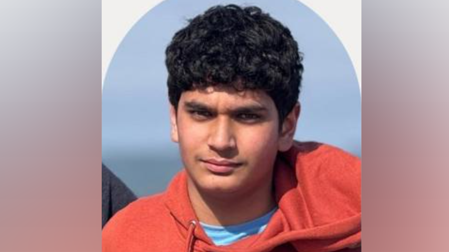 Nischay Patel had short, wavy black hair and wore a red hooded top, while standing in front of the sea.