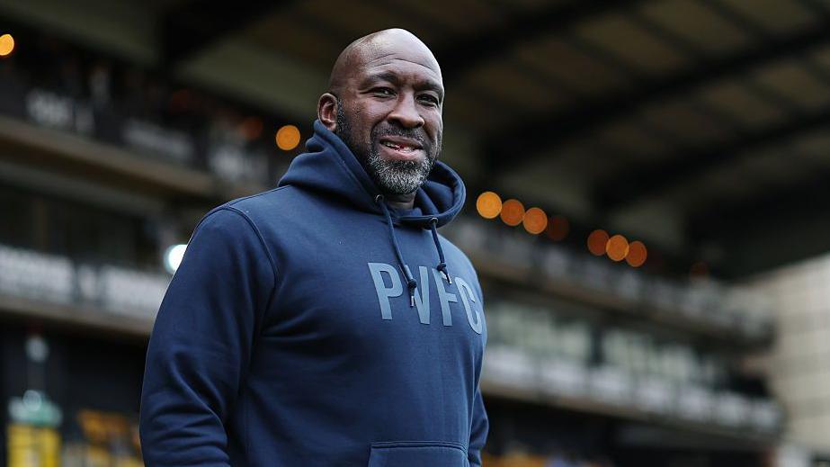 Darren Moore stands in his navy blue hoodie with the the letters PVFC on the front watching on from the touchline
