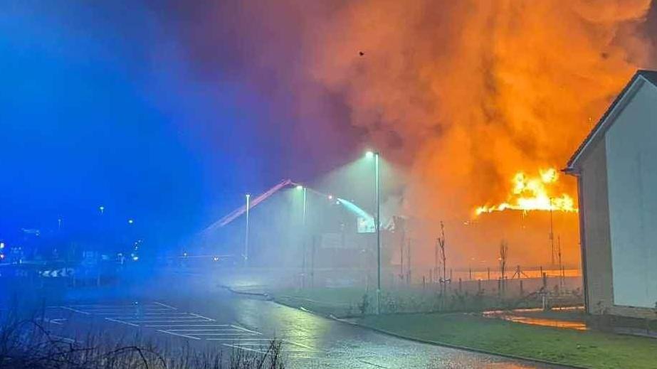 Orange flames nearby to residential houses with clouds of smoke rising into the air