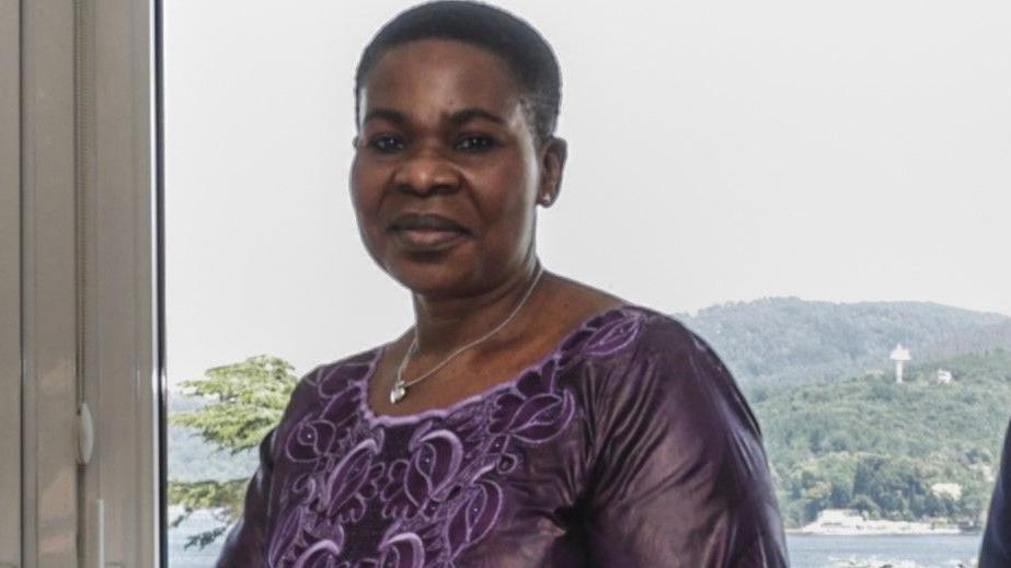 Marguerite Gnakade. She has cropped hair, and is wearing a purple open-necked dress and silver necklace.
