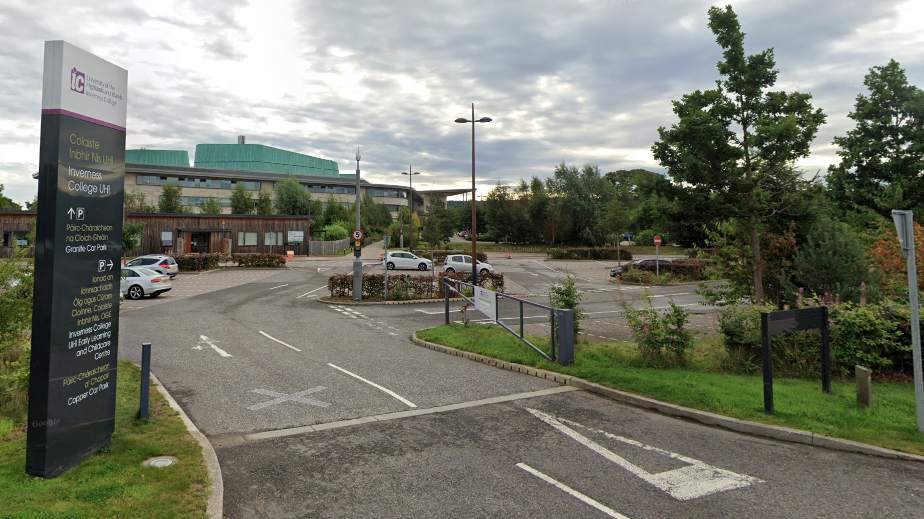 An outside shot of Inverness College UHI looking across a car park towards the college building. There is a sign at the entrance to the car park giving directions to different parts of the site.
