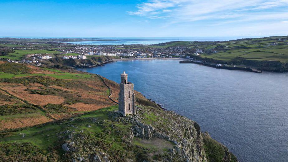 An aerial view of Milner's Tower, which stands on a clifftop on Bradda Head with the sea and Port Erin Bay in the background.