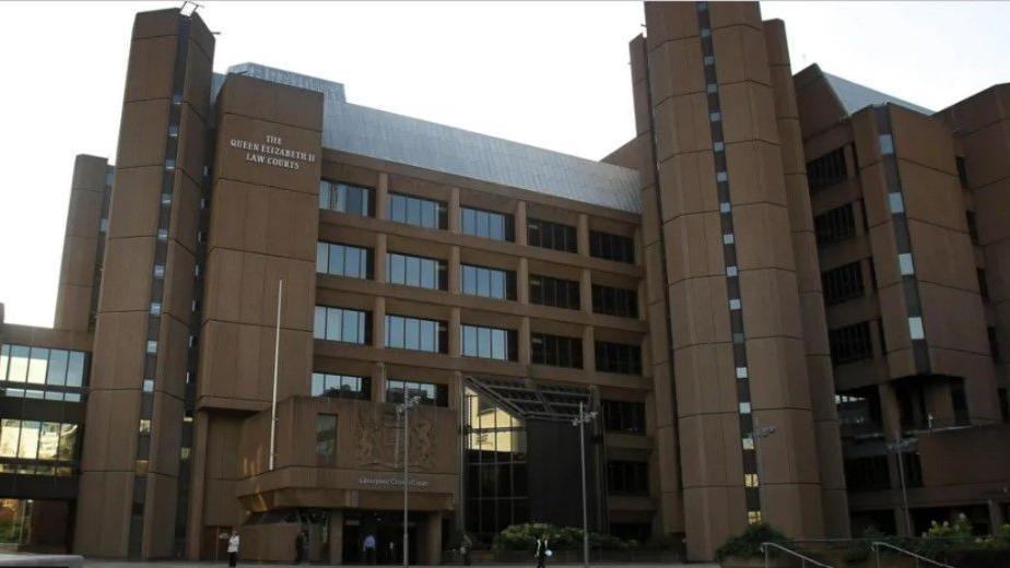 The exterior of Liverpool Crown Court, with some people seen outside the entrance and the words 'The Queen Elizabeth II Law Courts' on the outside of the building.