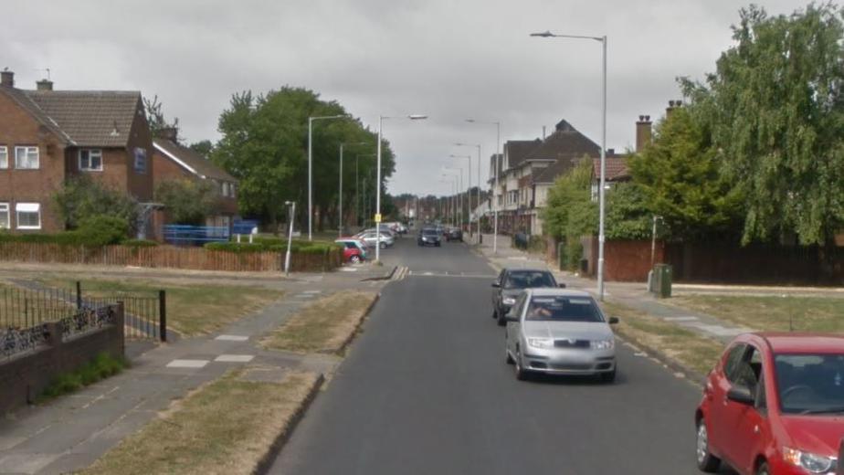 Cars driving down Hoole Road, lined with grassy sections and houses