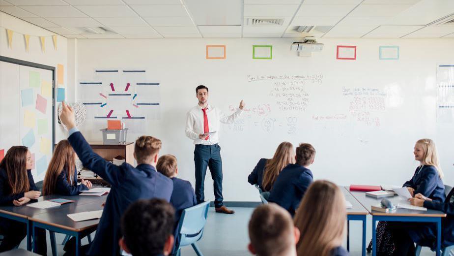 A school classroom with a teacher pointing to a white board