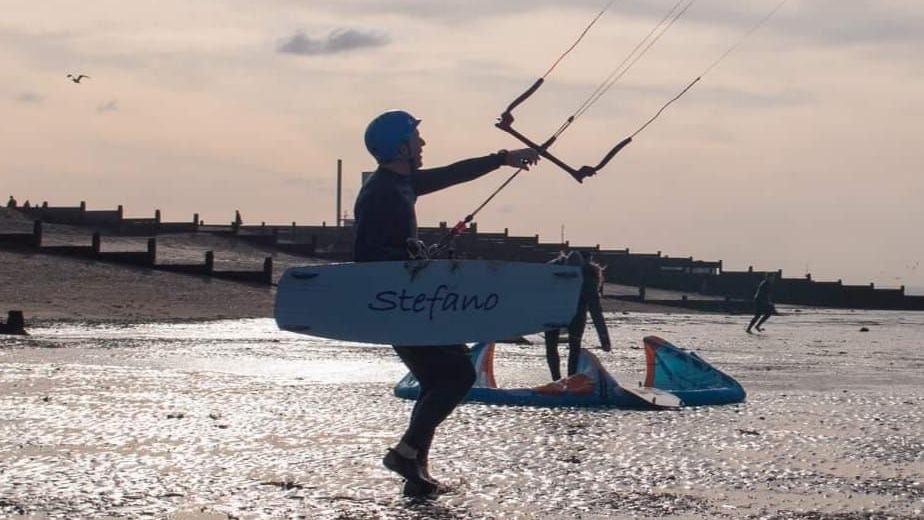 A kitesurfer is on a sandy beach in silhouette. 